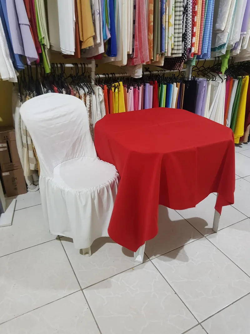 Mesa de quatro lugares com toalha vermelha e cadeira encapada, na loja do Grajaú